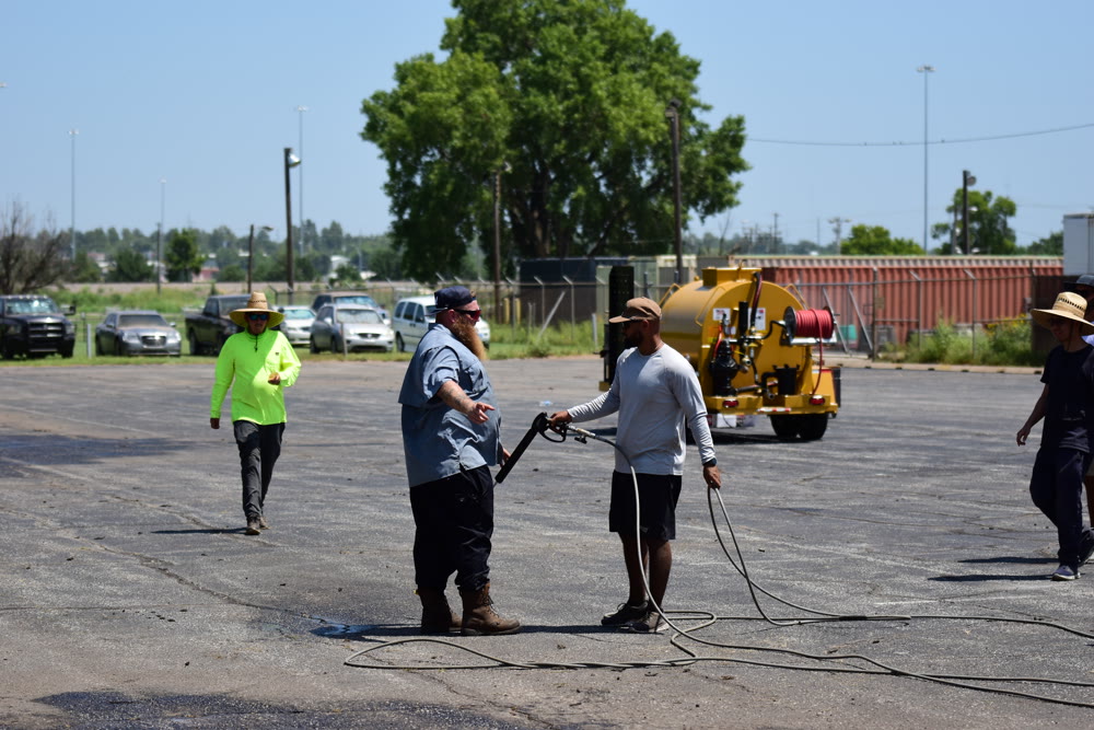 Crew applying sealcoat with a spray rig across a commercial parking lot
