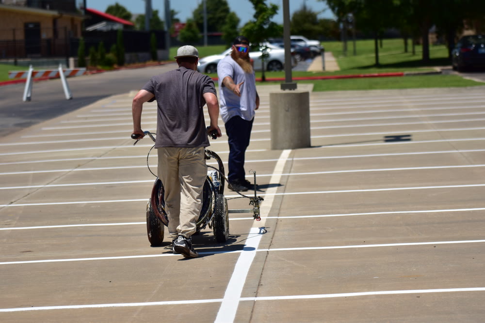Trainee pushing a striping machine laying fresh parking lot lines in daylight